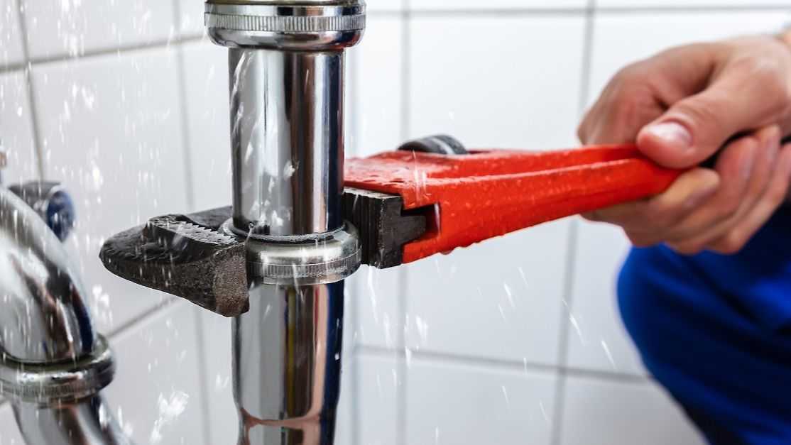 Alguien trabajando con una llave de tubo en el sifón de un lavabo.